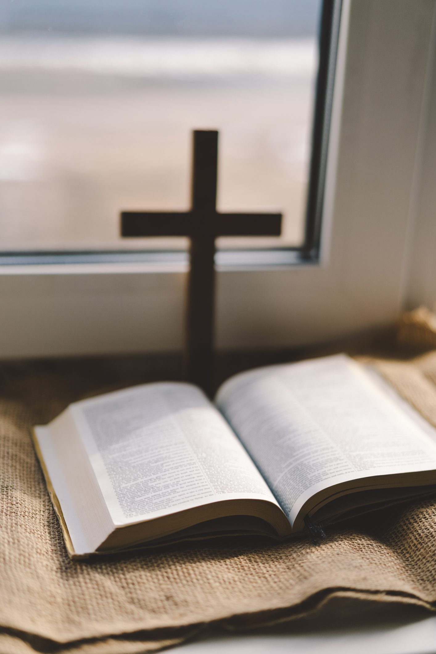 Open Bible by window with wooden cross