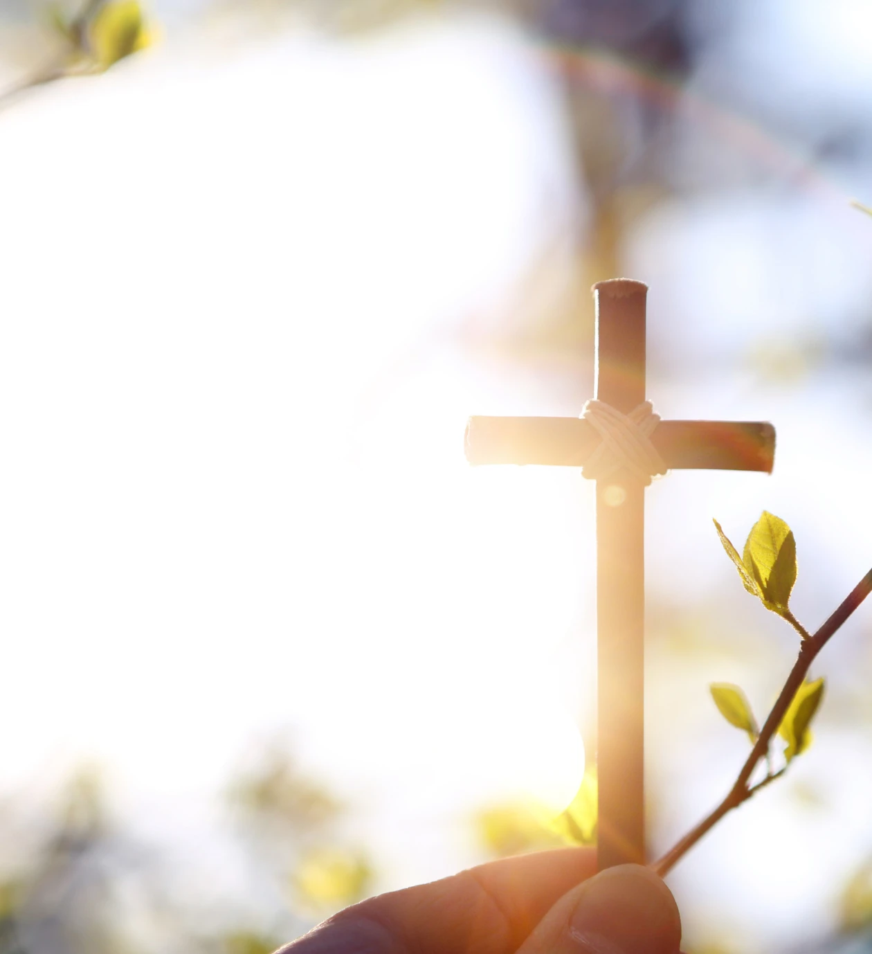 Hand holding cross against bright sunlight
