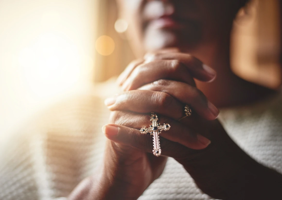 Close-up of hands clasped with cross.